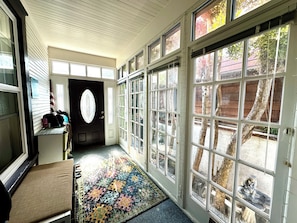 A hallway with a patterned rug, a black door with an oval window, and large windows with a view of trees and a brick wall. - Adorable Venice home in sought after Silver Triangle - walk to everything! (Los Angeles)
