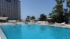 Une piscine entourée d’un bâtiment et d’arbres, avec des chaises longues et des parasols.