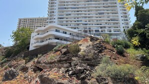 Un immeuble à plusieurs étages doté de balcons, situé sur un versant rocheux et entouré de végétation.