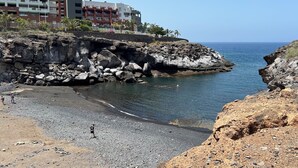 Une zone côtière caractérisée par un terrain rocheux, une plage et un bâtiment doté de nombreux balcons.