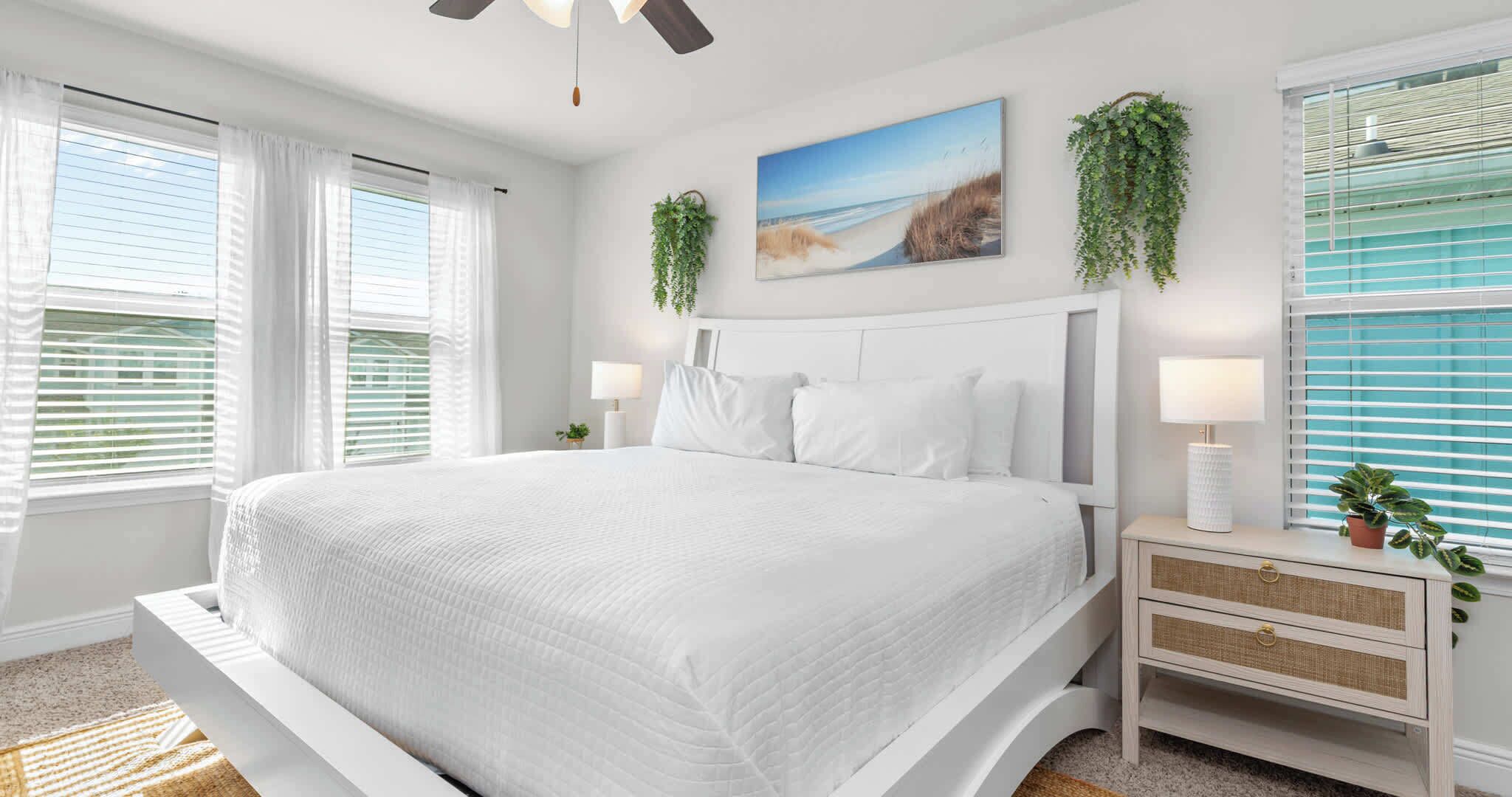 A bedroom with a large bed, white bedding, a nightstand with a lamp, and a wall-mounted plant.