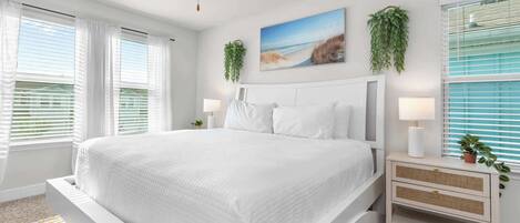 A bedroom with a large bed, white bedding, a nightstand with a lamp, and a wall-mounted plant.