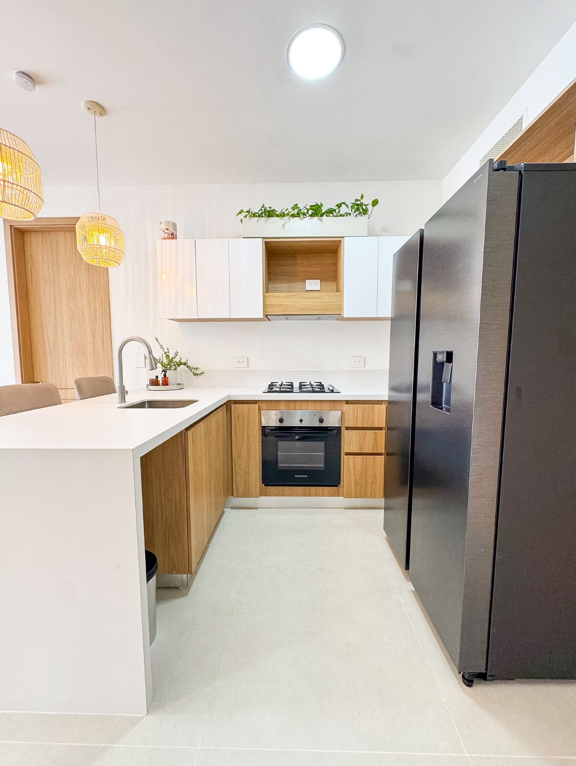 Een moderne keuken met een centraal eiland, inbouwoven, koelkast van roestvrij staal en hanglampen.