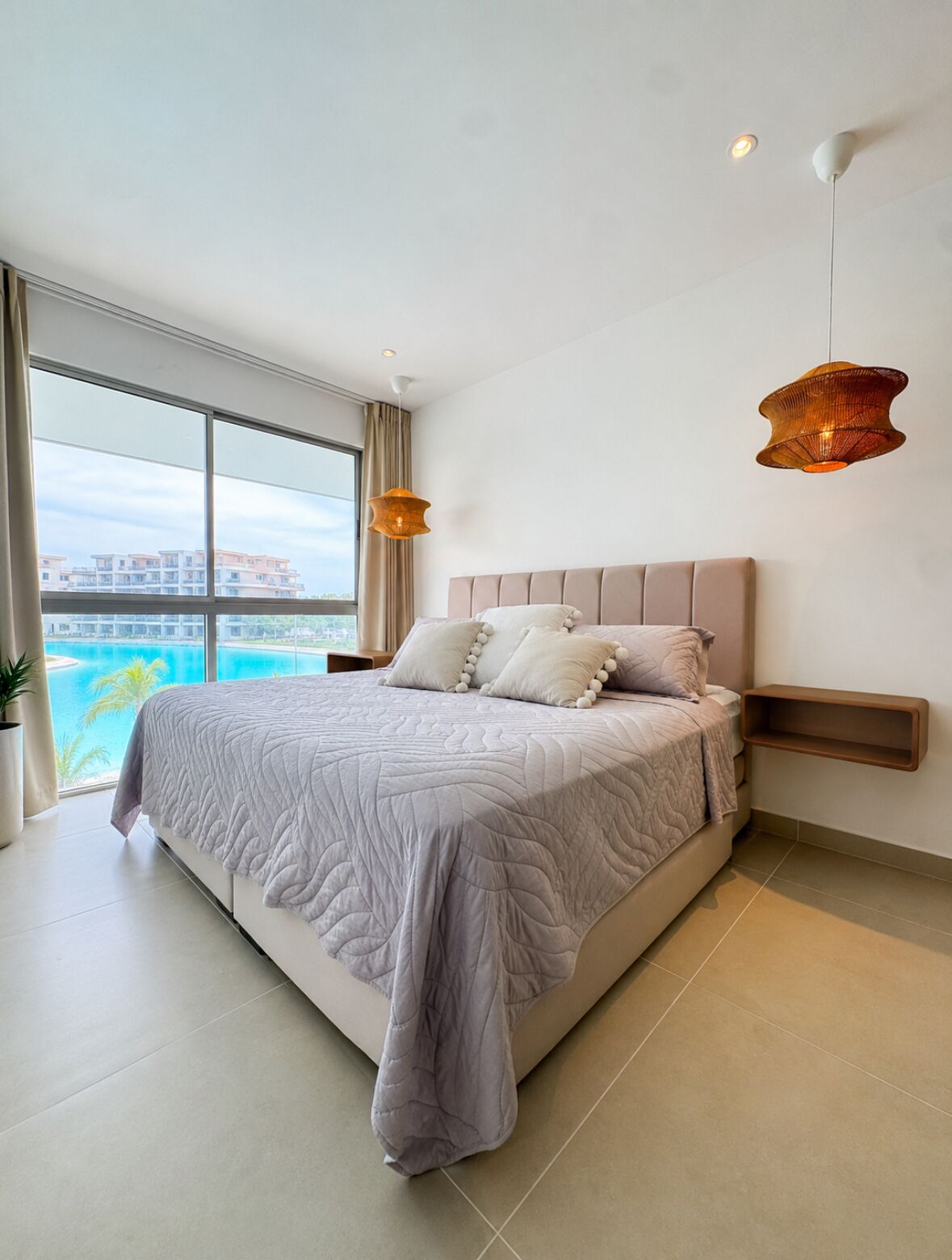 A modern bedroom with a large bed, a view of a body of water, and two pendant lights.
