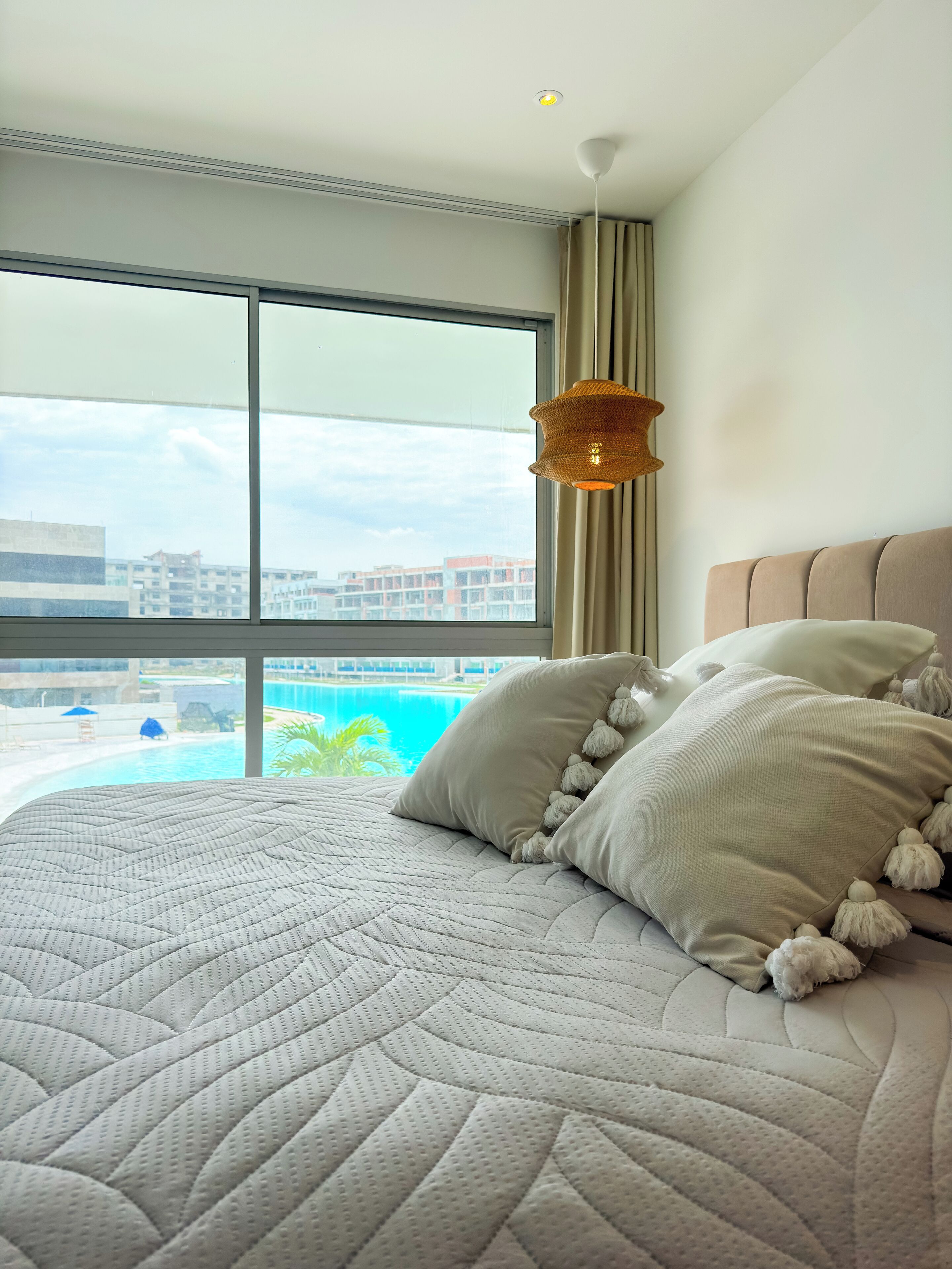 Habitación de hotel con una cama grande, vista a una piscina y una lámpara colgante.