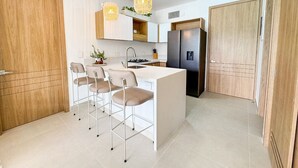 Een moderne keuken met een centraal eiland, barkrukken, hanglampen en een inbouwkoelkast.