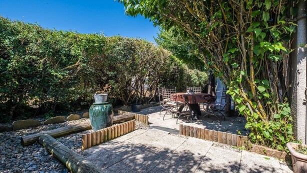 A patio area with a table and chairs, surrounded by dense foliage and a large green vase. - Alyxia's Villa - LA BASTIDE-PUYLAURENT (LA BASTIDE-PUYLAURENT)