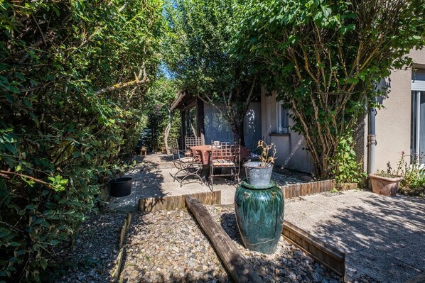 A garden with a wooden bench, a table, and a large green vase.
