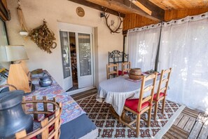 A rustic room with a wooden table, chairs, a patterned rug, and a door leading to an outdoor area.