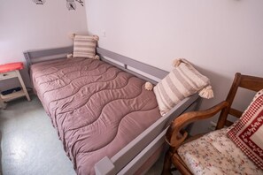 A single bed with a pink quilt, two pillows, a wooden chair with a floral cushion, and a small bedside table with a red cushion. - Alyxia's Villa - LA BASTIDE-PUYLAURENT (LA BASTIDE-PUYLAURENT)