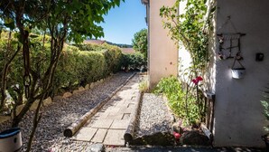A pathway leading to a building with a garden area, a wall with hanging flower baskets, and a clear sky. - Alyxia's Villa - LA BASTIDE-PUYLAURENT (LA BASTIDE-PUYLAURENT)