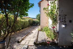 A pathway leading to a building with a garden area, a wall with hanging flower baskets, and a clear sky. - Alyxia's Villa - LA BASTIDE-PUYLAURENT (LA BASTIDE-PUYLAURENT)