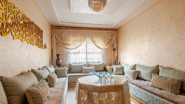 A spacious living room with a large sofa set, a round coffee table, and a decorative wall piece. - Elegant family 2br flat, secure 24/7, quiet area (Tangier)
