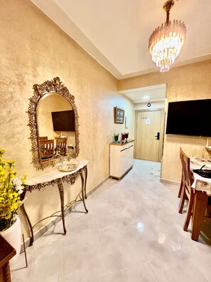 A dining area with a chandelier, a large ornate mirror, and a television. - Elegant family 2br flat, secure 24/7, quiet area (Tangier)