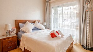 A hotel room with a bed, a nightstand, a lamp, and a window with curtains. - Elegant family 2br flat, secure 24/7, quiet area (Tangier)