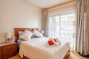 A hotel room with a bed, a nightstand, a lamp, and a window with curtains. - Elegant family 2br flat, secure 24/7, quiet area (Tangier)