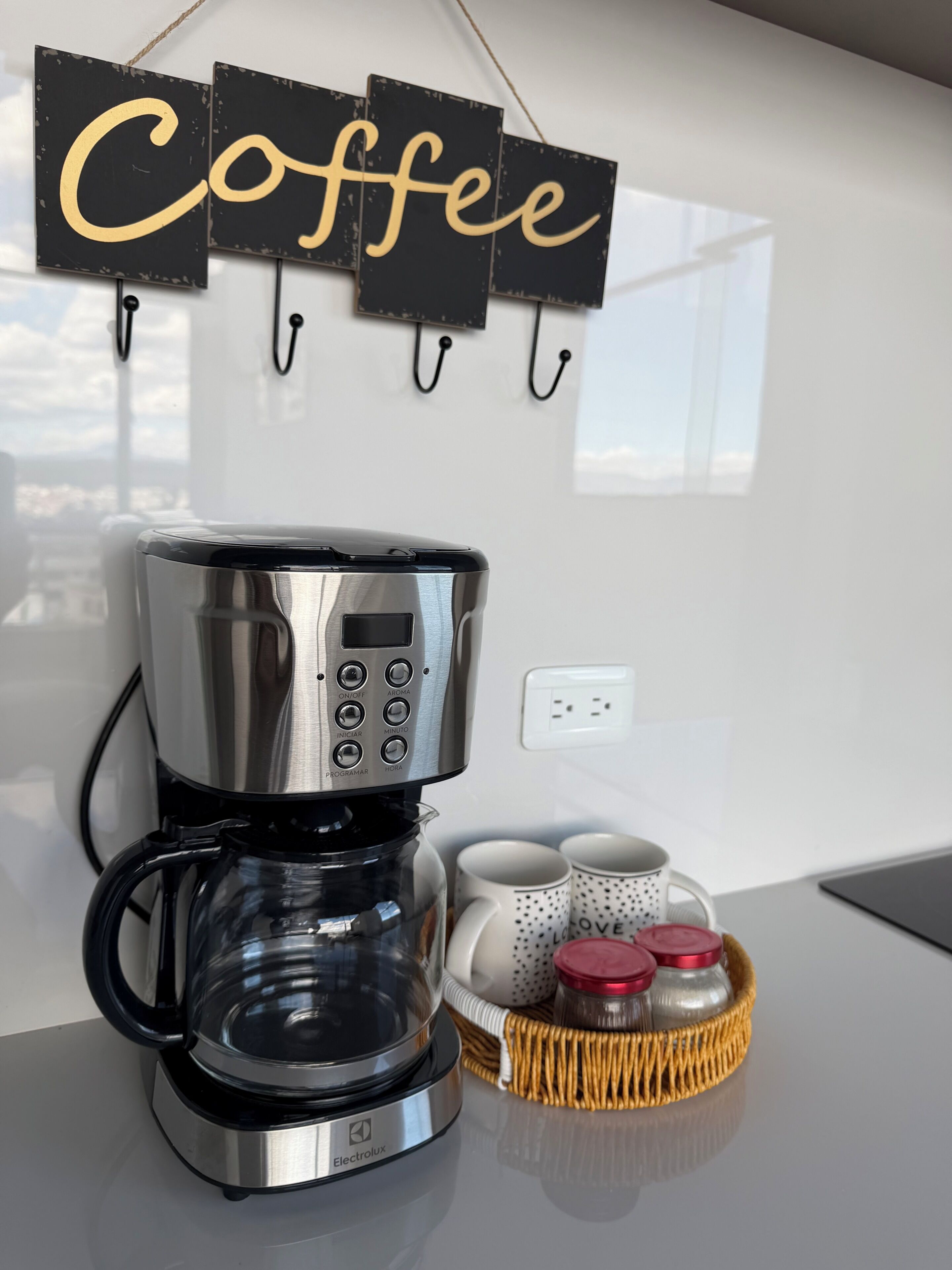 Eine Kaffeemaschine mit digitaler Anzeige, ein Tablett mit Tassen und ein Schild mit dem Schriftzug 'Coffee'.