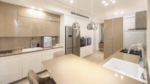 Une cuisine moderne dotée d’un îlot central, d’appareils électroménagers en acier inoxydable et de luminaires suspendus.