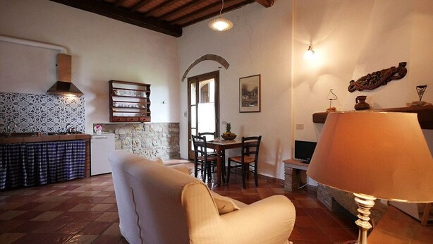 A cozy living room with a sofa, a dining table with chairs, a lamp, a fireplace, and a kitchen area with a stove and cabinets. - Villa Opera - Apartment in Massa Carrara (Toscana)