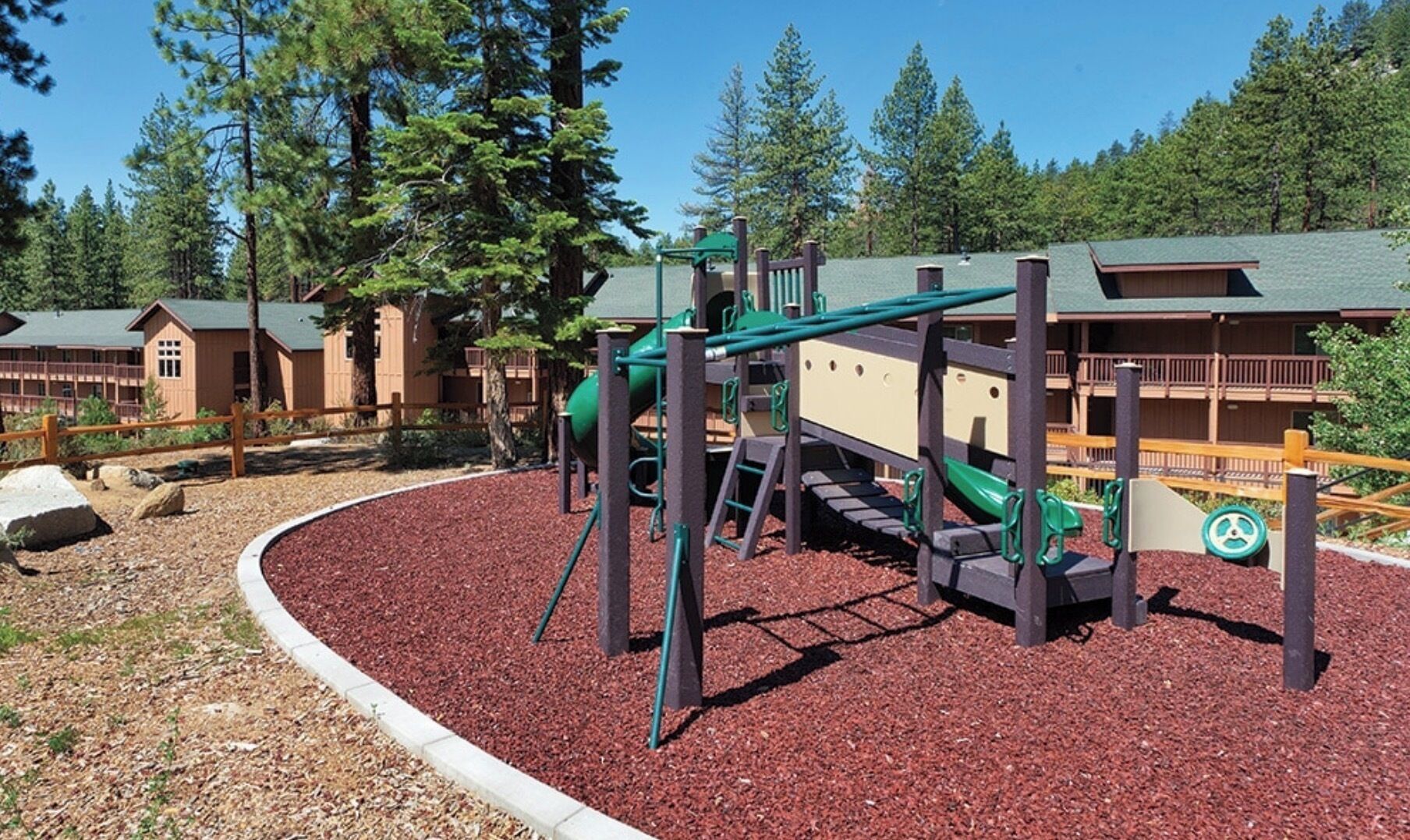 A playground with a swing set and climbing structures, surrounded by a red mulch area and a wooden fence. - Wyndham South Shore Resort condo in Zephyr Cove with kitchen and more! (Zephyr Cove)