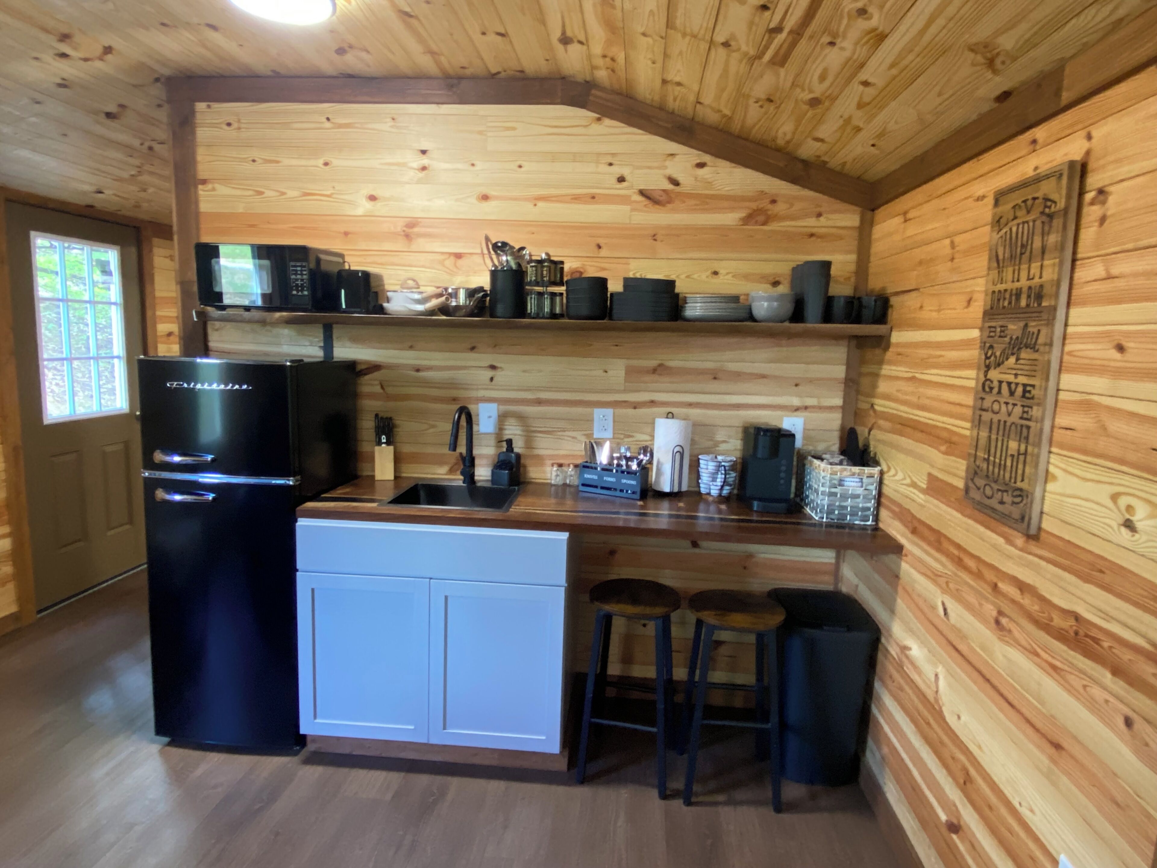 A compact kitchen with a refrigerator, sink, and bar stools.