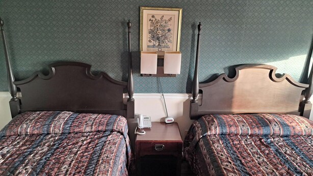 Habitación de hotel con dos camas, una mesita de noche con teléfono, e ilustración botánica enmarcada en la pared.