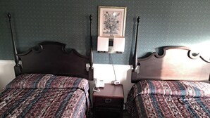 Una habitación con dos camas, una mesita de noche con teléfono y una lámpara fijada a la pared.