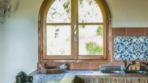 A kitchen with a large arched window, a tiled backsplash, and a countertop with a basket and a camera.