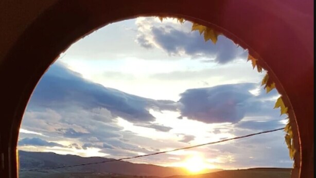 A view through an arched window of a sunset over a hilly landscape.