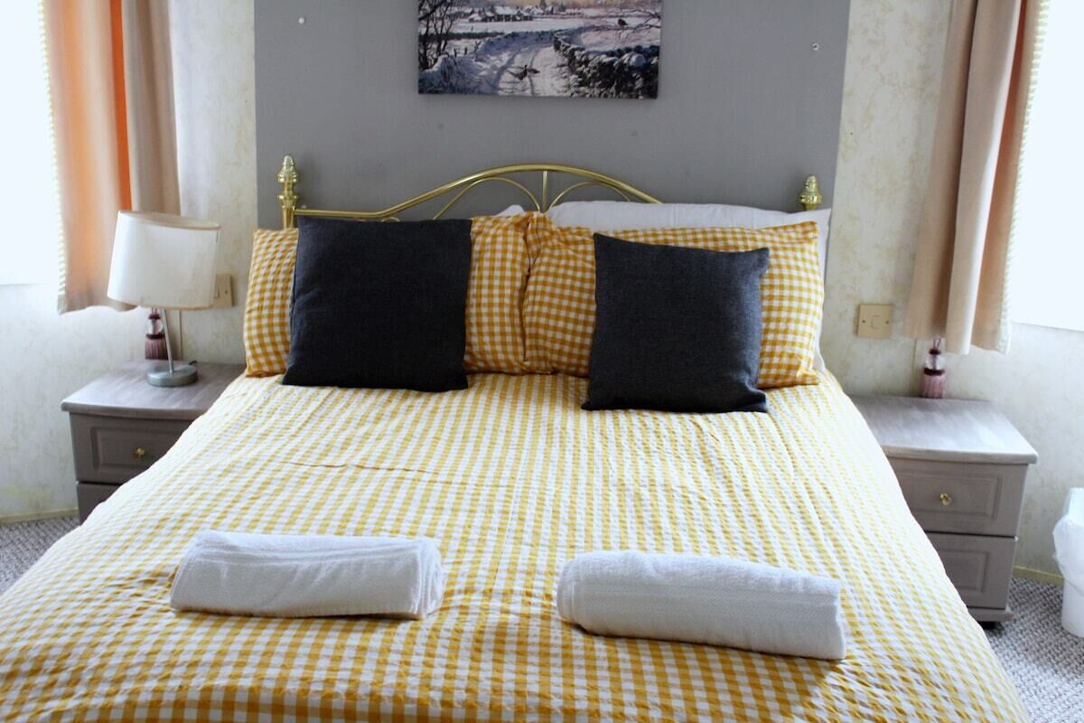Uma cama com colcha xadrez, duas almofadas, duas mesas de cabeceira com luminárias e um quadro na parede.