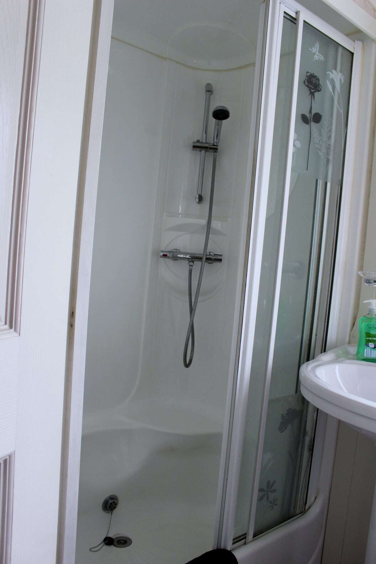 Cabina de ducha con puerta de vidrio, cabezal de ducha de mano y grifo empotrado en la pared.