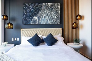 Ein modernes Schlafzimmer mit einem großen Bett, zwei Wandlampen, einem Holz-Kopfteil und einem Wandbild.