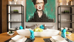 Zona pranzo con un'ampia pittura, un tavolo in legno apparecchiato per un pasto e due scaffali neri con oggetti decorativi.