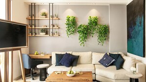 Un soggiorno moderno con un divano, un tavolino da caffè e una TV. Si vedono scaffali con piante e un grande quadro appeso al muro.