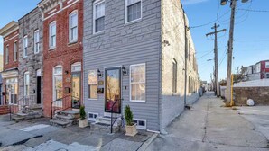 A row of townhouses with a grey facade, a visible number '2313' on the front, and a small front yard with steps leading to the entrance. - Spacious 3-bedroom Townhome in Superb Baltimore Location with AC and Comfort (Baltimore)