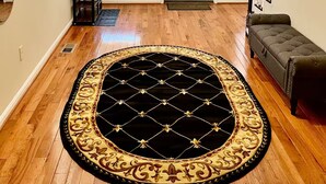 A hallway with a wooden floor, a black and gold rug, a door, and a staircase. - Spacious 3-bedroom Townhome in Superb Baltimore Location with AC and Comfort (Baltimore)