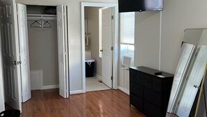 A spacious room with hardwood flooring, a flat-screen TV mounted on the wall, and a walk-in closet with hanging space. - Spacious 3-bedroom Townhome in Superb Baltimore Location with AC and Comfort (Baltimore)