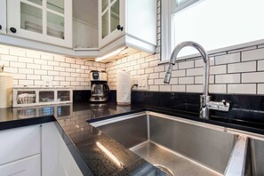 Eine Küche mit einer Spüle aus Edelstahl, einer Kaffeemaschine und einem Fenster über der Spüle.