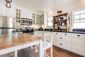 Eine moderne Küche mit weißen Schränken, einem Edelstahl-Kühlschrank, einer Mikrowelle und einem Holzespeisetisch mit Stühlen.