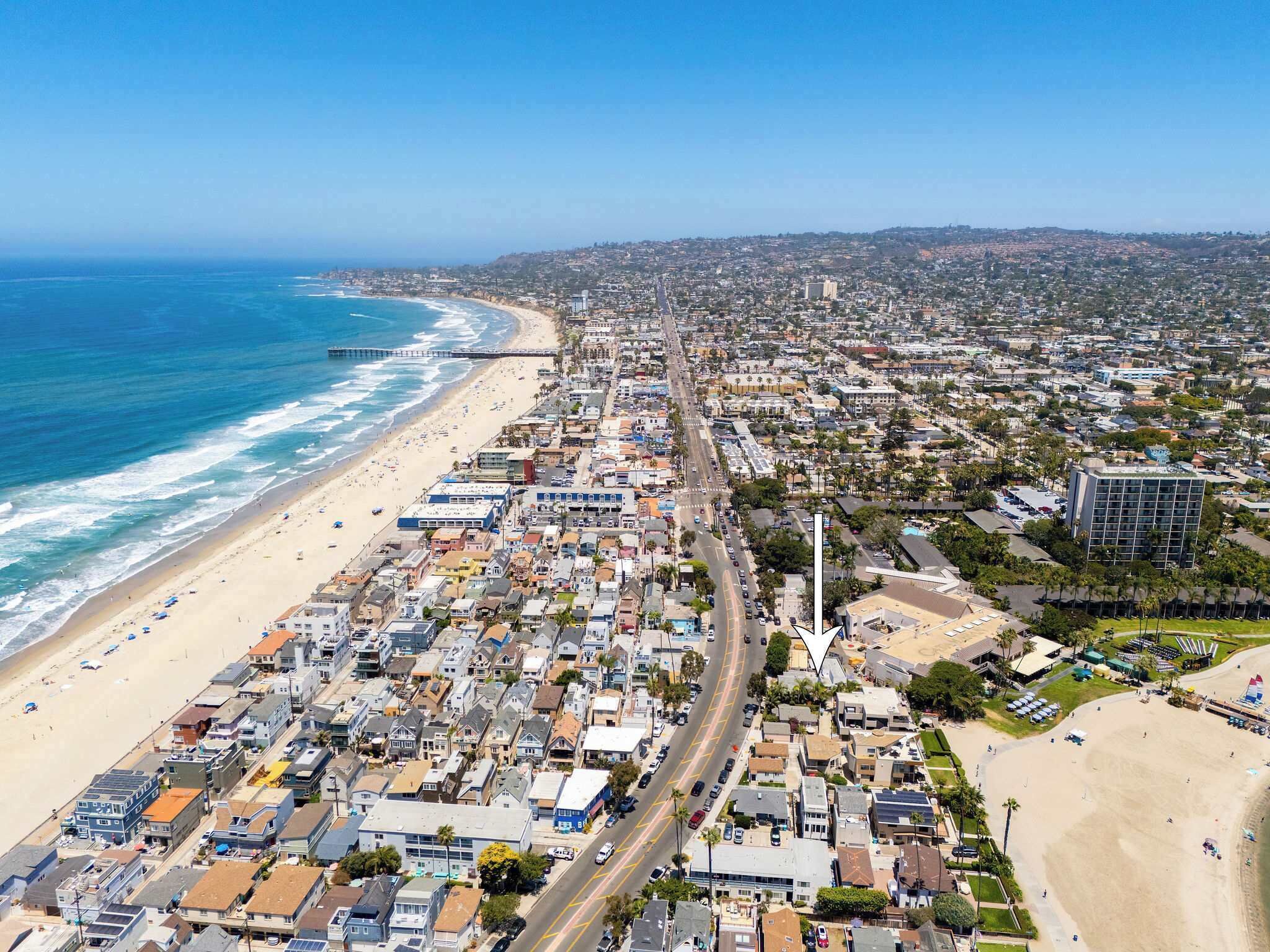 Un paysage urbain côtier comprenant une plage, une zone résidentielle densément peuplée et un phare imposant.