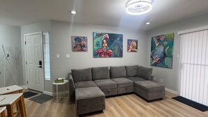 Een moderne woonkamer met een hoekbank, houten vloeren en abstracte wanddecoratie.