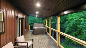 Eine überdachte Terrasse im Freien mit Holzgeländern, einem Whirlpool und Sitzgelegenheiten.