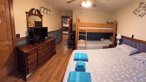 A bedroom with a wooden bed, a dresser, a television, and a ceiling fan.