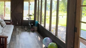 A room with a wooden floor, a sofa, a bicycle, and a view of greenery outside.