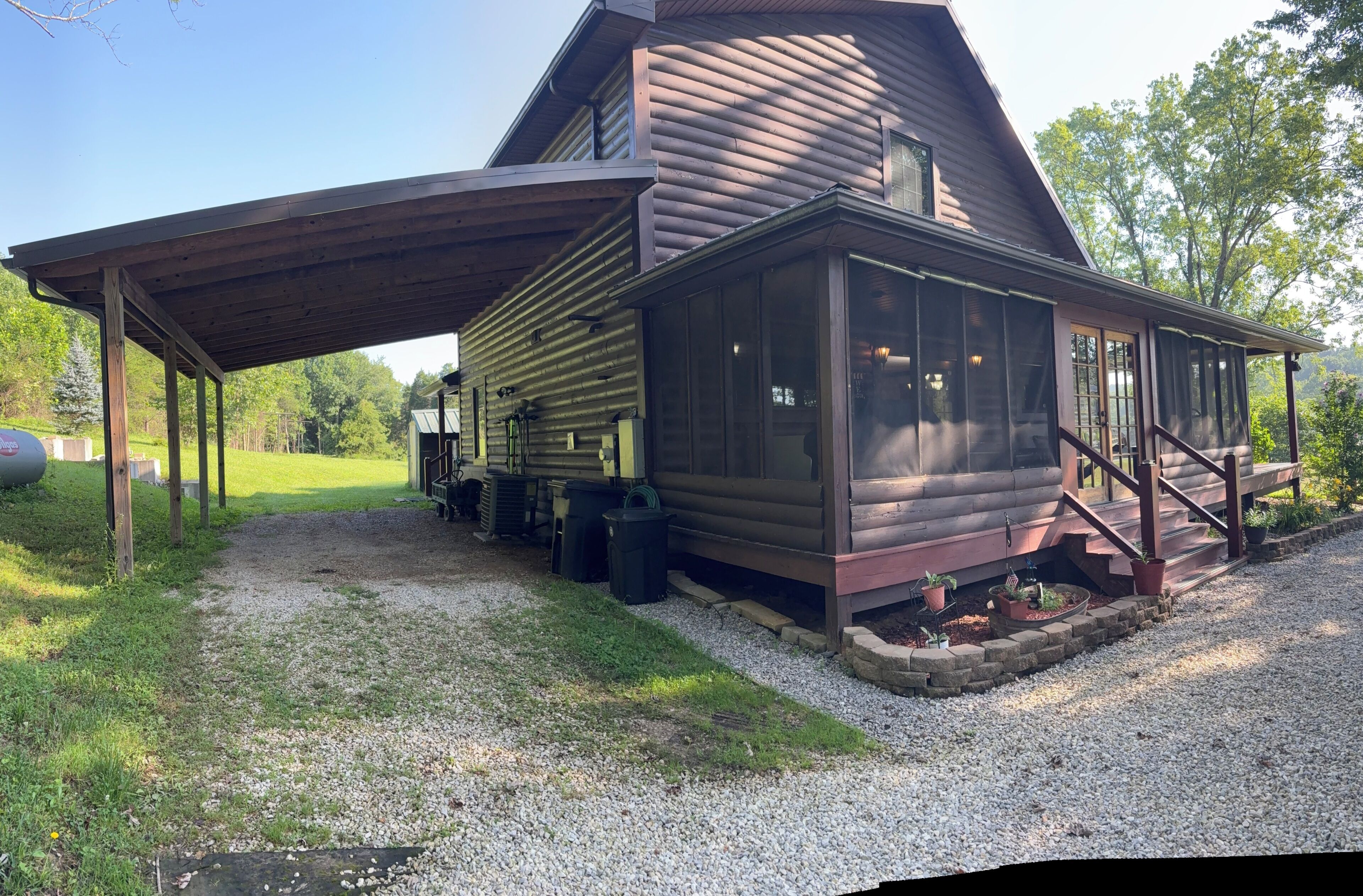 Une cabane en rondins dotée d’un porche couvert, d’une entrée avec des marches et d’une allée en gravier.