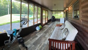 A covered porch with a wooden bench, exercise equipment, and a view of a green landscape.