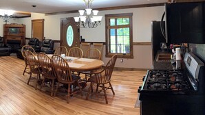 A spacious dining area with a wooden table and chairs, a chandelier, and a kitchen with a stove.