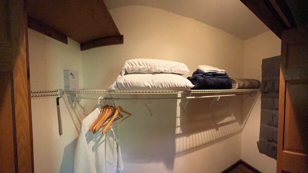A small, enclosed room with a bunk bed, a hanging clothes rack, and a wooden floor.