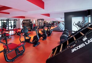 Ein Fitnessraum mit unterschiedlichen Trainingsgeräten, einem roten Boden und einem Schild mit der Aufschrift 'Wellness Zone'.