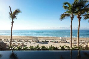 Vista da praia com palmeiras, espreguiçadeiras e uma piscina.